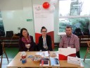 Trzy osoby Przedstawiciele Urzędu Skarbowego w Malborku siedzący na tle baneru biało czerwonego z napisem KAS Krajowa Administracja Skarbowa poniżej Izba Administracji Skarbowej w Gdańsku